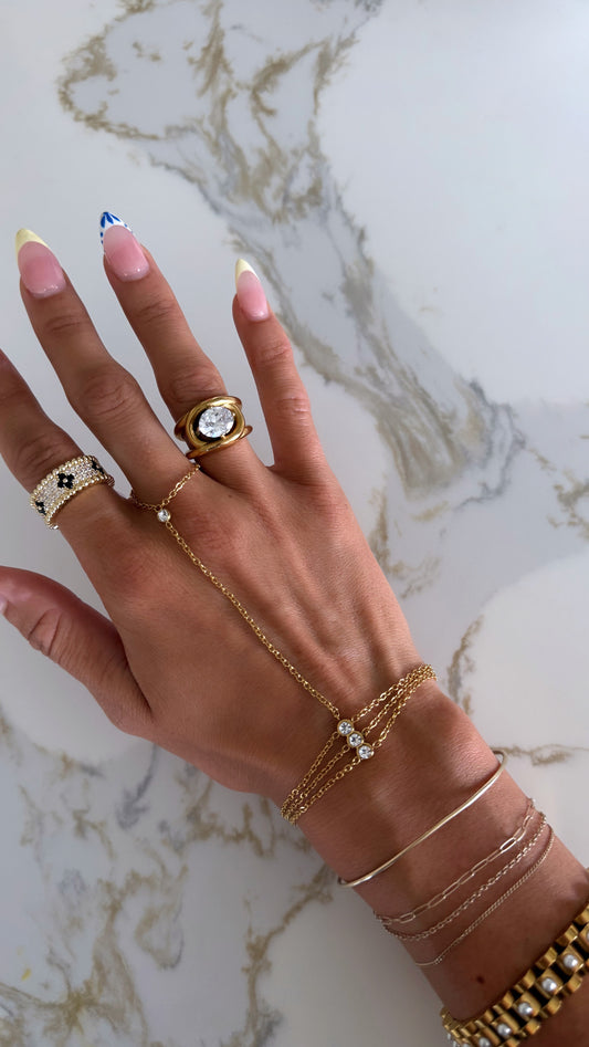 Hand wearing multiple gold rings and bracelets on a marble background